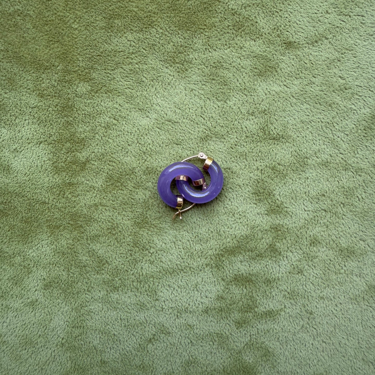 Small lavender jade hoops with 14k gold metal details, placed on a textured olive green surface.