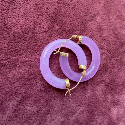A pair of lavender jade hoop earrings with 14k gold hooks, displayed on a textured mauve fabric background.
