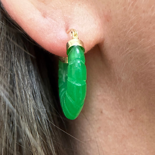 A close-up of a model's ear wearing a green jade leaf-shaped gold hoop earring.