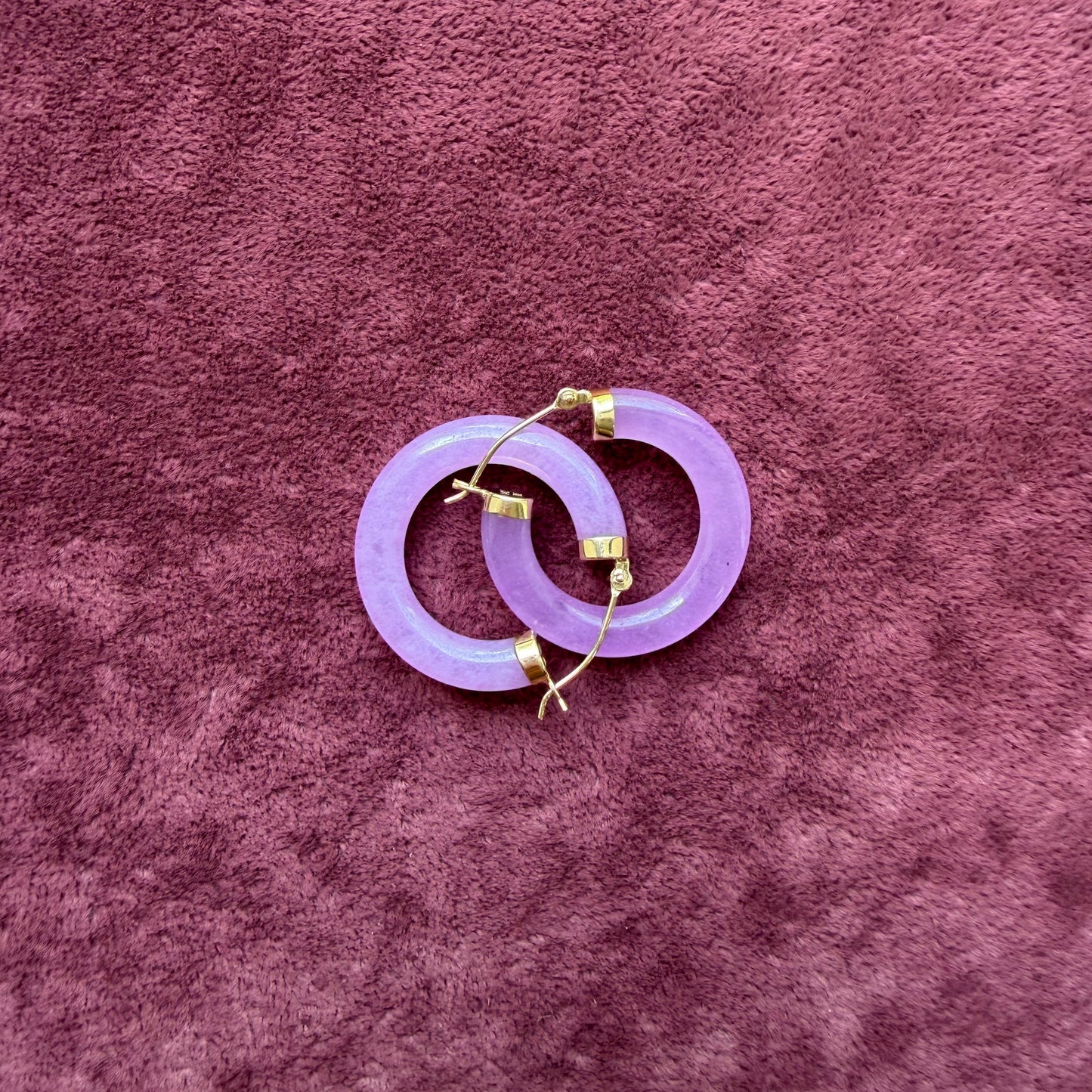 Two lavender jade hoops with 14k gold hooks, arranged on a textured mauve velvet background.