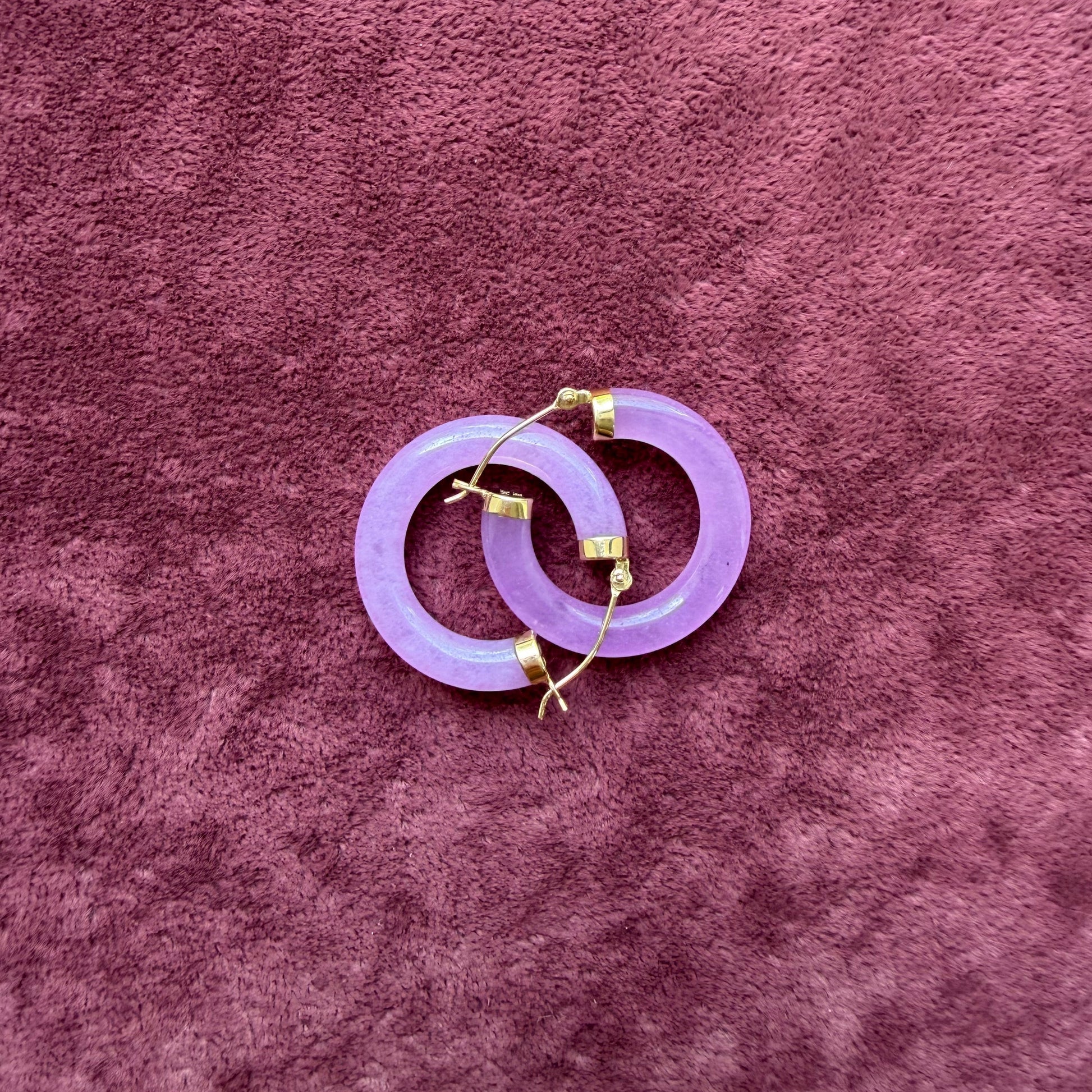 Two lavender jade hoops with 14k gold hooks, arranged on a textured mauve velvet background.