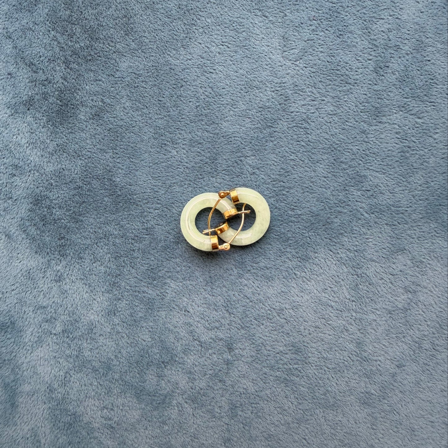 A small light green jade hoop, photographed on a textured dark blue-gray surface.
