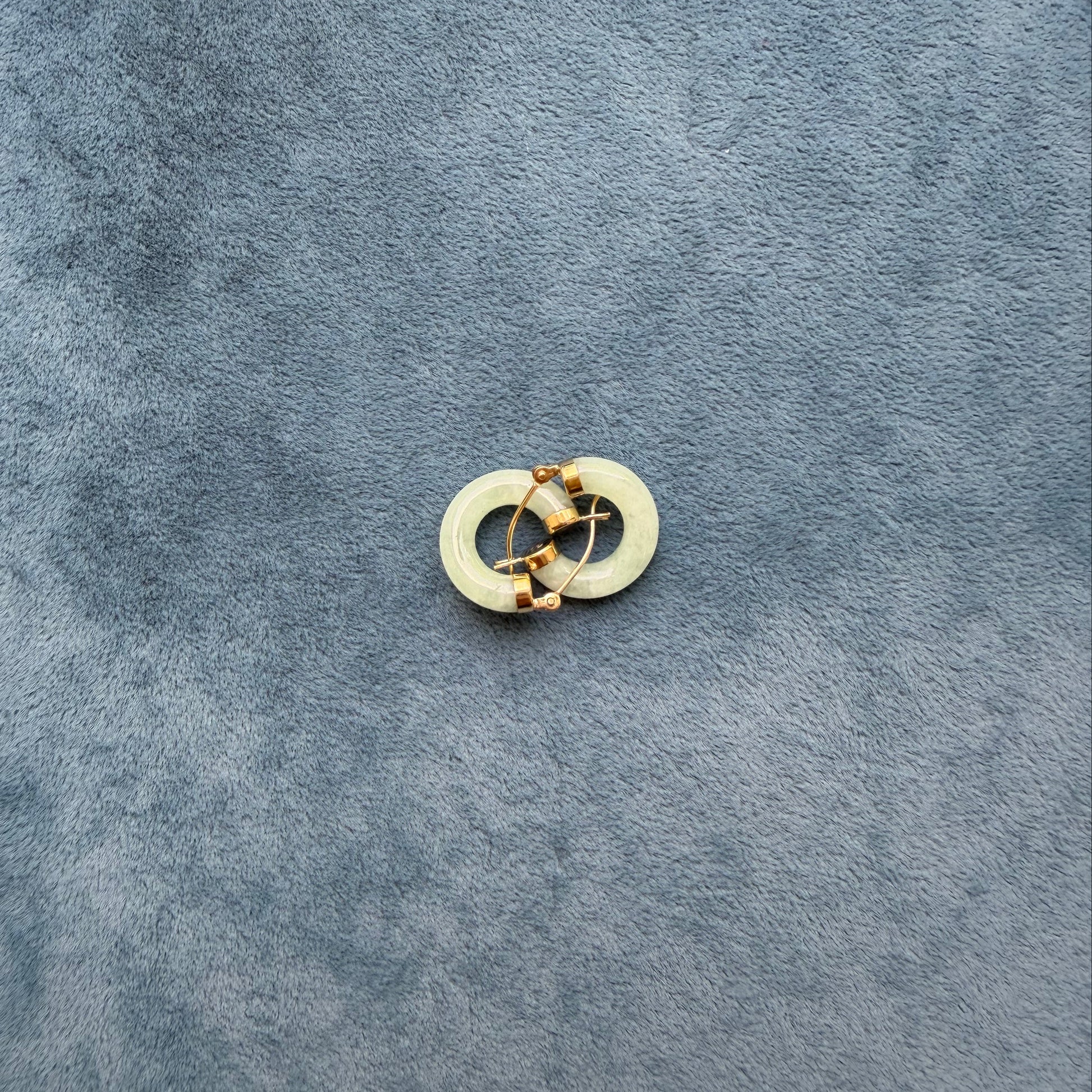 A small light green jade hoop, photographed on a textured dark blue-gray surface.