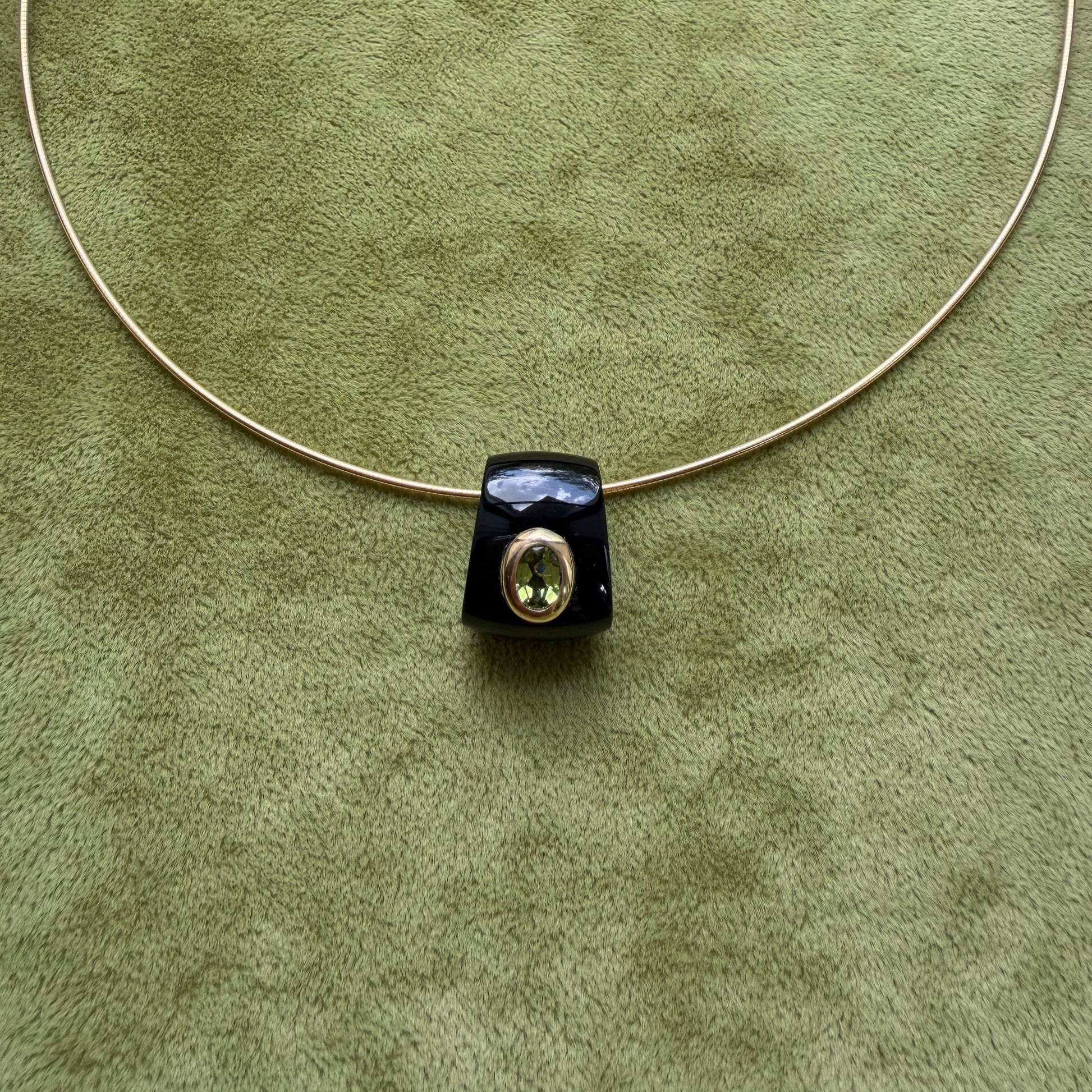 A black onyx pendant featuring a central peridot, displayed on a textured olive green background.