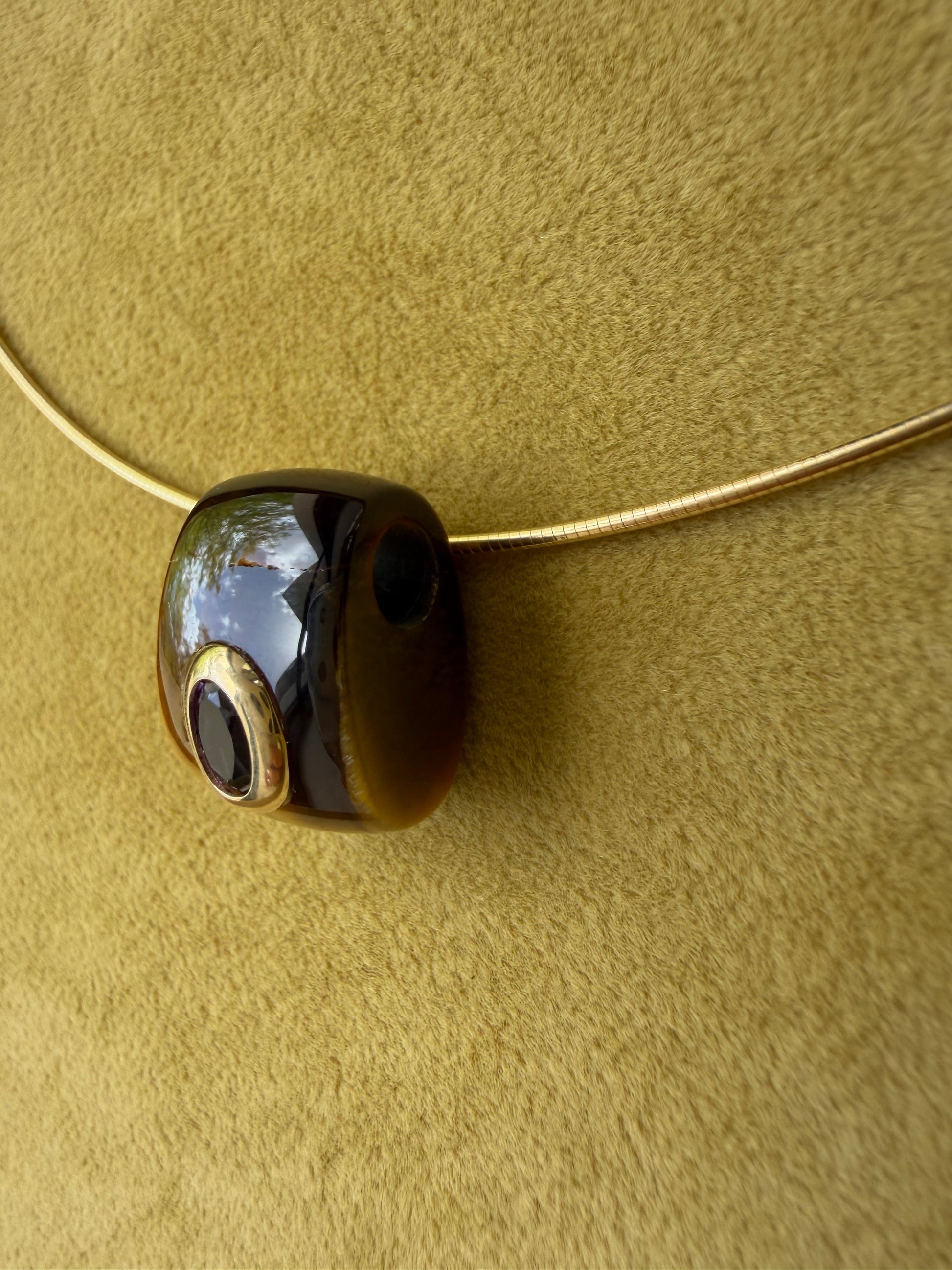 Side view of a tiger's eye pendant featuring an amethyst bezel in 14k gold.