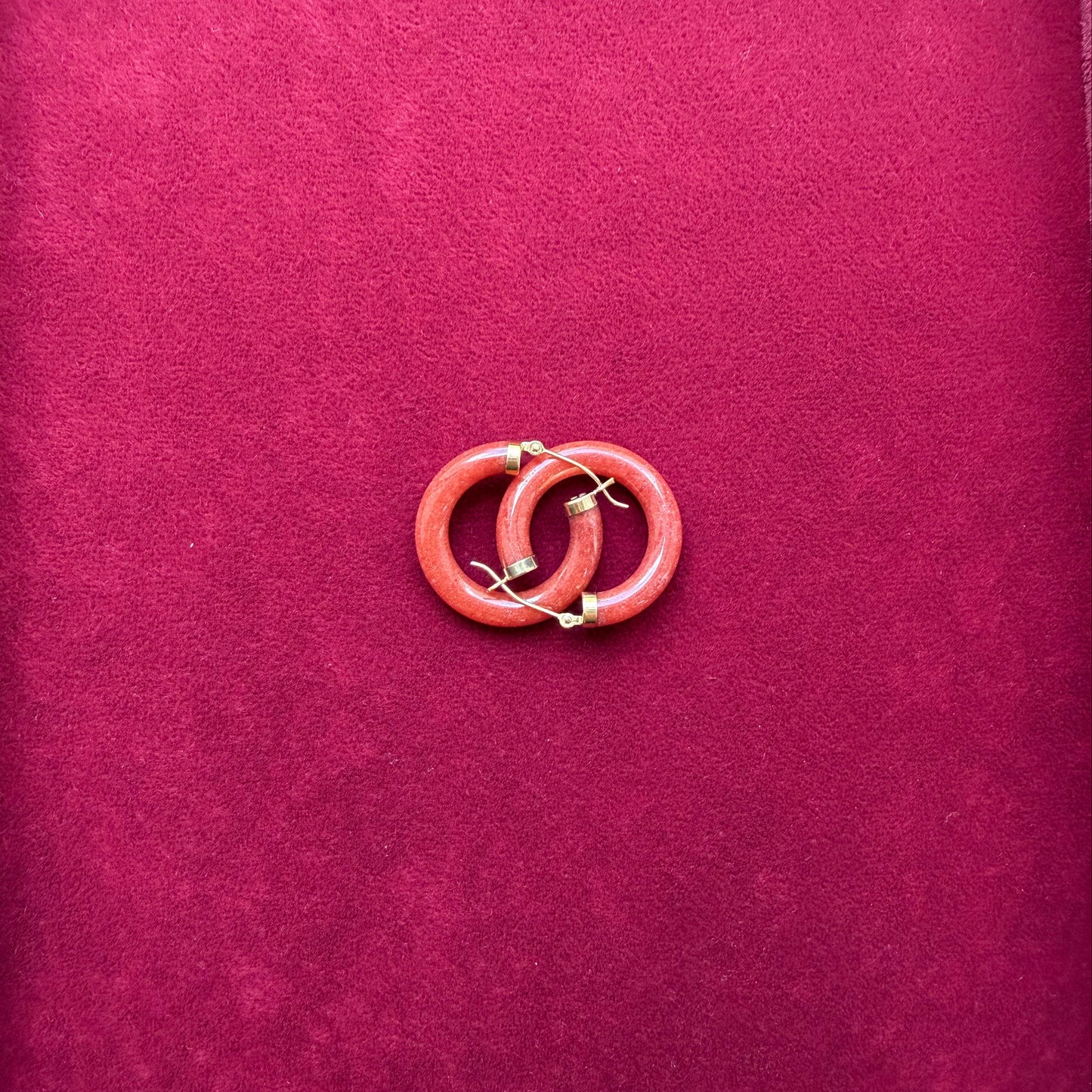 A pair red jade and 14 gold hoop earrings displayed on a textured magenta velvet surface.
