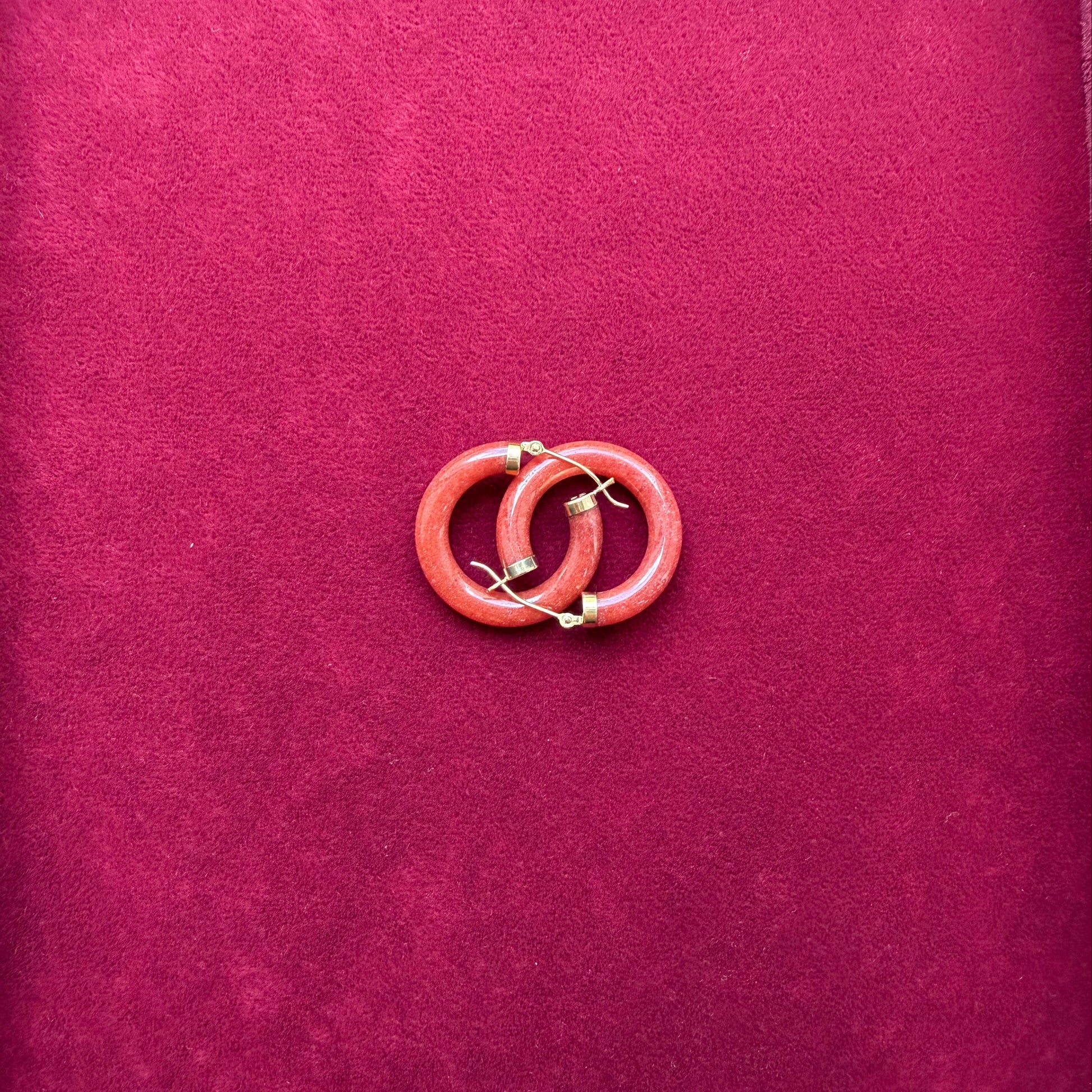 A pair red jade and 14 gold hoop earrings displayed on a textured magenta velvet surface.