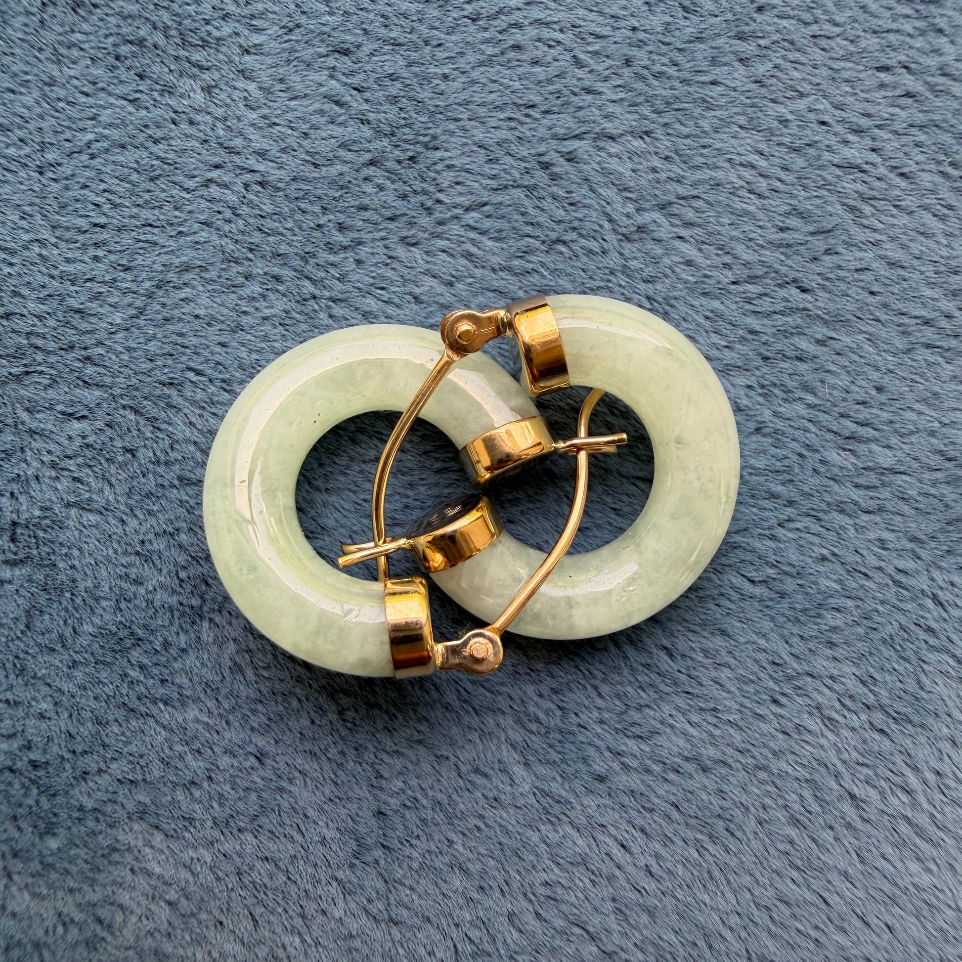 Light green jade hoops with 14k gold metal clasps, displayed on a textured blue-gray fabric background.