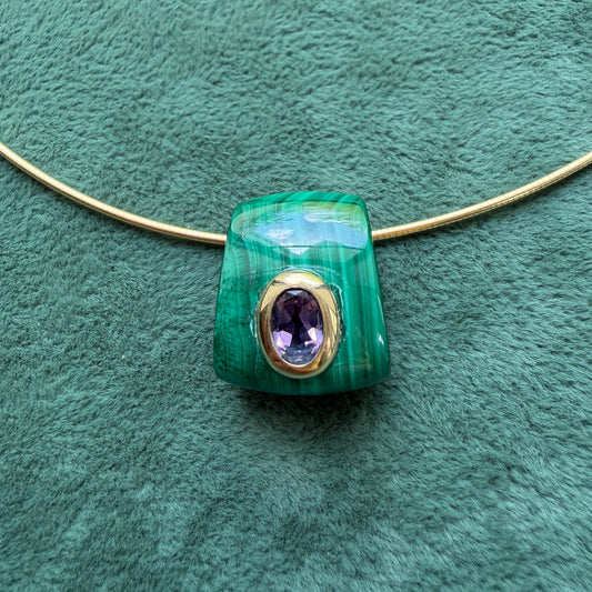 A malachite pendant with and a central oval amethyst gemstone, displayed on a textured green background.