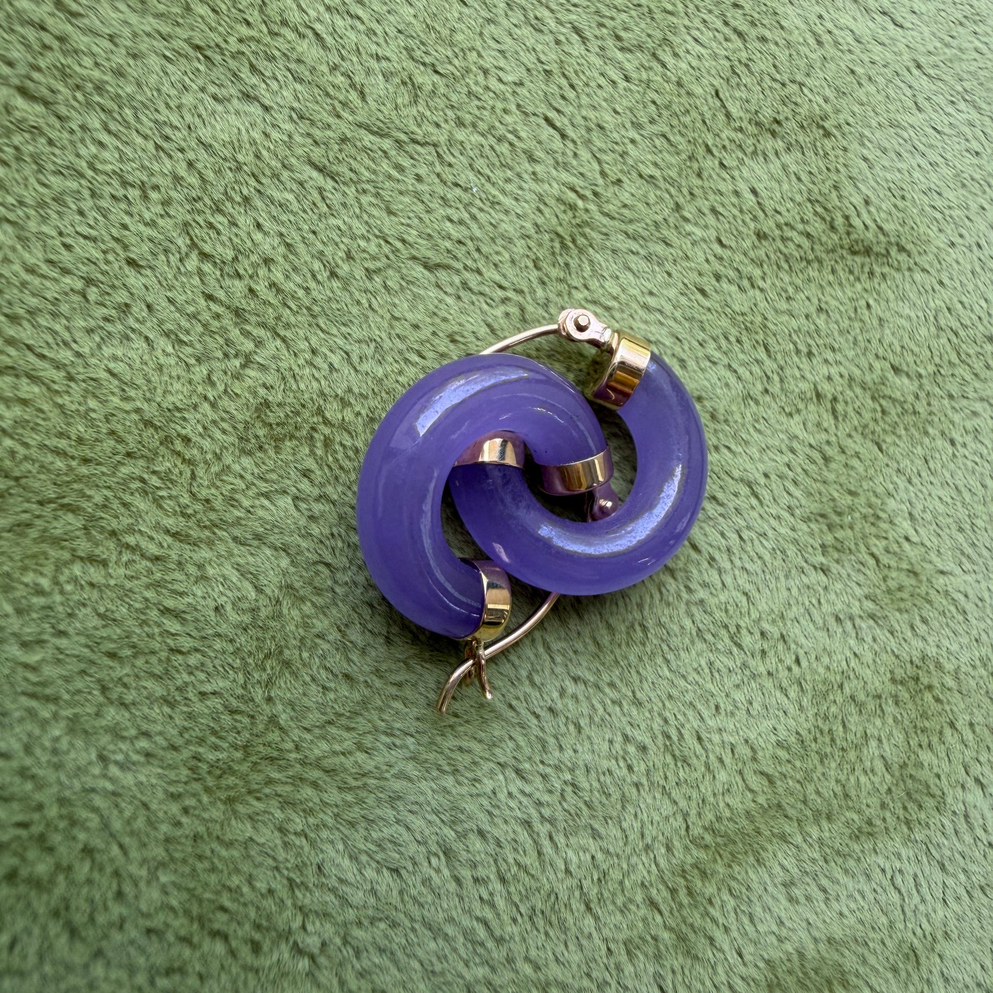 Lavender jade hoops with 14k gold hooks, placed on a textured green fabric background.