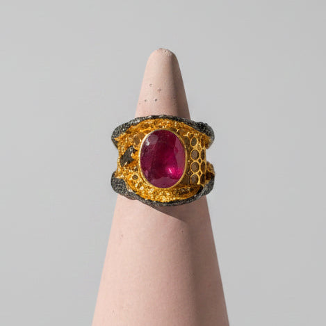 A gold ring with a large oval pink ruby, accompanied by an accent emerald stone.