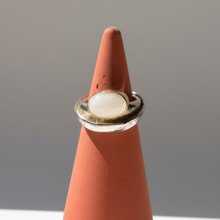 Folded oval moonstone ring set in silver with warm brass accents.