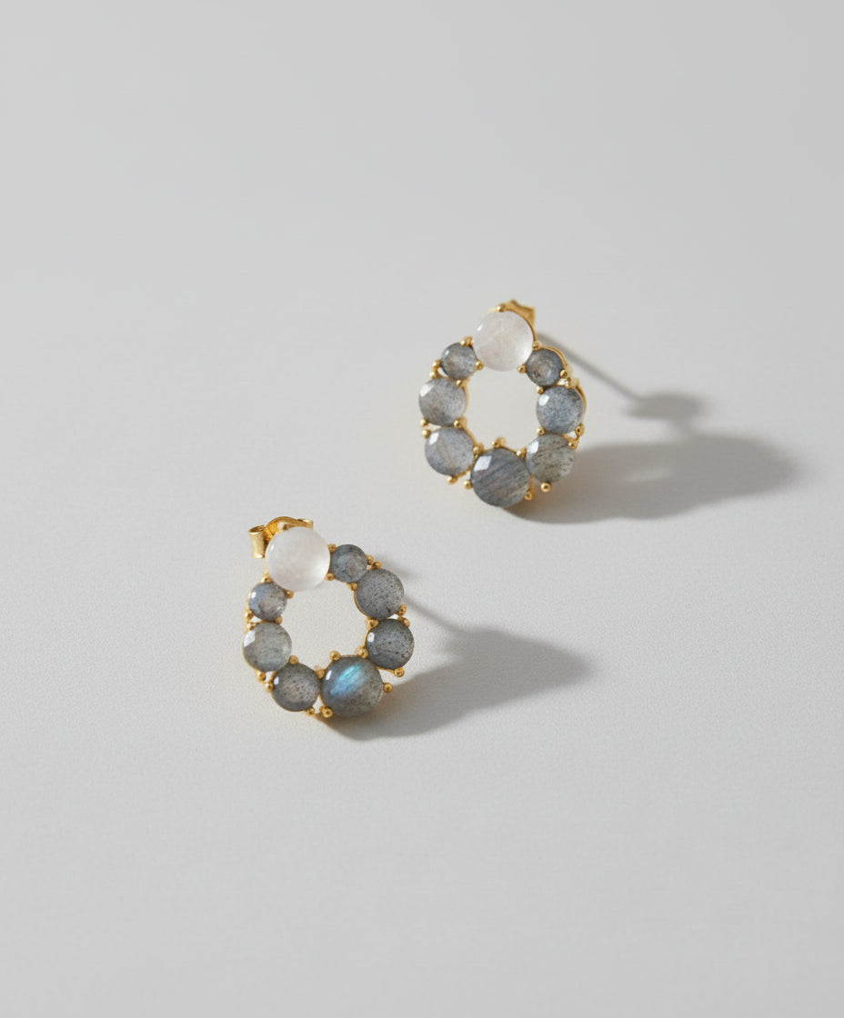 A pair of gold-plated brass labradorite stud earrings with rainbow moonstone accents, displayed against a brown background.